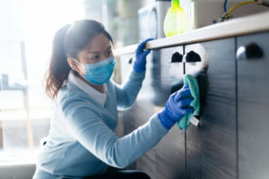 female wearing protective face mask cleaning home with disinfectant wipe