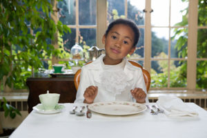 Girl sitting at table setting, smiling 