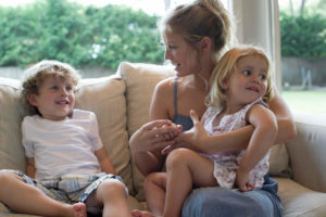 Nanny and two young children sitting together on sofa